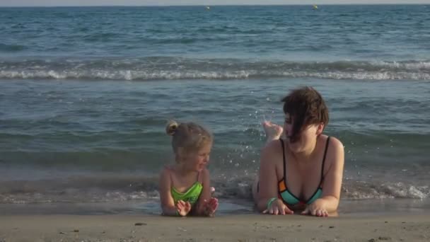 Mãe e filha deitam-se de barriga na praia e penduram os pés — Vídeo de Stock