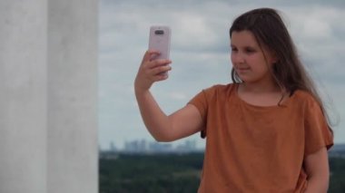 Brunette teen girl in a brown t-shirt makes selfie on the phone