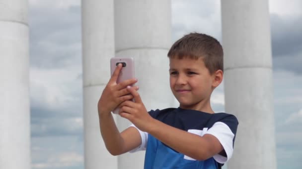 Boy makes selfie on the phone against the sky and the colonnade — 图库视频影像