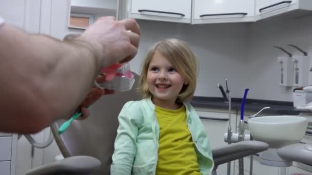 Dentist shows to a little girl a jaw model to explain how to brush teeth — Stock video