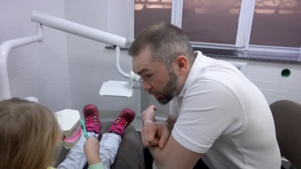 Dentist explains to a little cute girl how to clean her teeth — Stock video