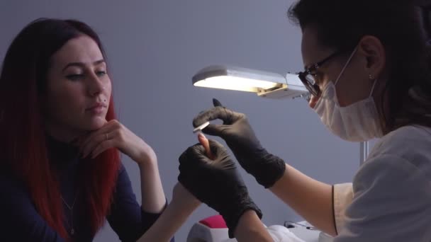 Manicure corrigeert een vorm van vingernagels van haar cliënt. — Stockvideo