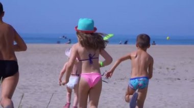 Five children in bright clothes run on the sand towards the sea 