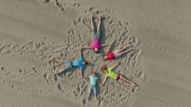 Children lie on the sand in the shape of a star and wave hands