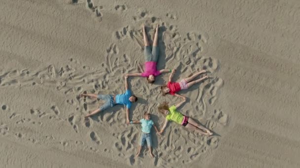 Los niños yacen en la arena en forma de estrella y saludan con las manos — Vídeos de Stock