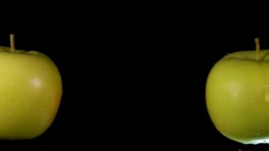 Two large green apples are colliding with each other on the black background