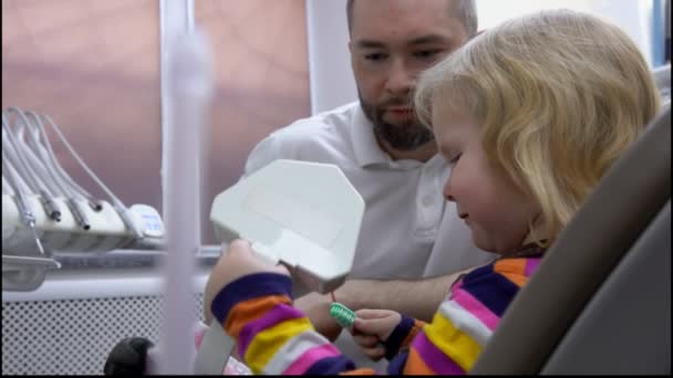 Il dentista spiega a una bambina come pulire i denti su un modello di mascella di plastica — Video Stock