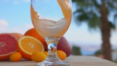 Multifruit suyu, palmiye ağaçlarının arka planına karşı şarap bardağına döküldü.