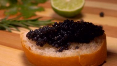 Close-up of a spoon pressing black caviar to the bread slice