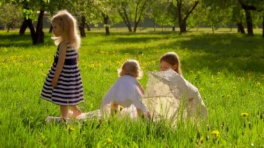 Three girls in beautiful striped dresses are playing in the garden with dog