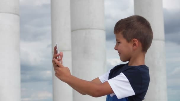 Boy makes selfie on the phone against the sky and the white colonnade — 图库视频影像