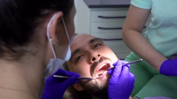 Dentist is examining the teeth of a male patient with a special dental mirror — Stok video