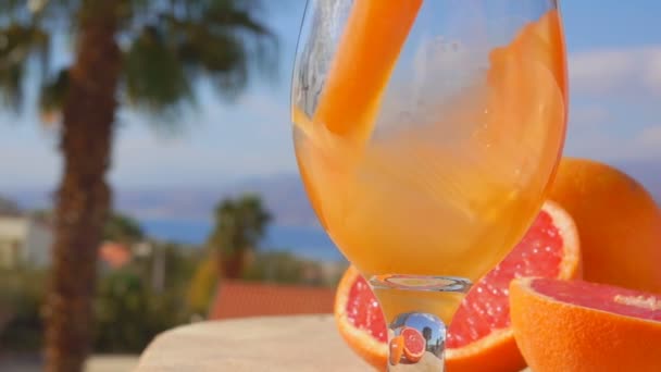 Крупный план грейпфрутового сока, налитого в стакан на фоне моря — стоковое видео