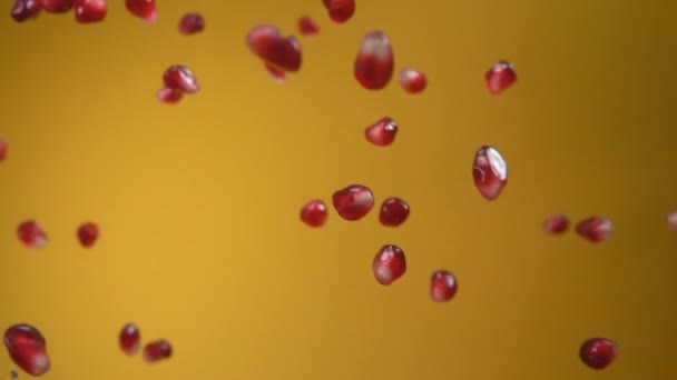 Saftiga korn av granatäpple faller diagonalt på den gula bakgrunden — Stockvideo