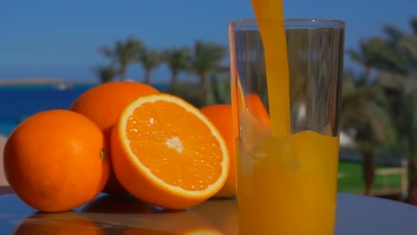 Färsk apelsinjuice hälls i ett glas i bakgrunden av havet landskapet — Stockvideo