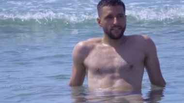 Young handsome man is sitting in the waves of the sea surf