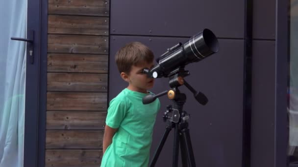 Маленький веселый мальчик рассматривает небо через телескоп — стоковое видео