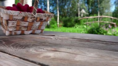 Bir sepet dolusu olgun kırmızı ahududu açık havada ahşap bir masaya düşüyor.