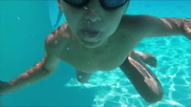 Çocuk havuza dalıyor ve komik suratlar yapmaya başlıyor, dilini gösteriyor.