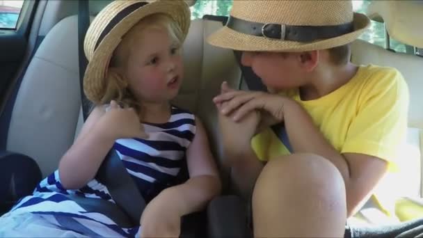 Liten pojke och en blond flicka i hattar rider i bilen vid baksätet — Stockvideo