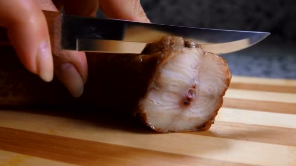 Vrouwelijke hand snijdt gerookte paling in plakjes met een mes — Stockvideo