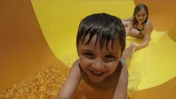Fiú és lány egy narancssárga csúszdán lovagolnak egy vízi parkban. — Stock videók