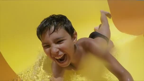 Laughing boy rides down orange slide on his stomach in a water park — Stock Video