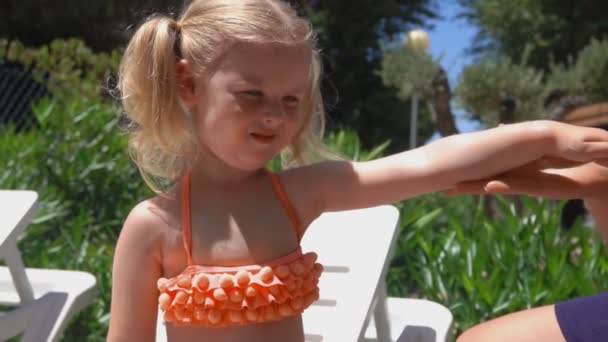 Kvinnlig hand smetar solskyddande kräm på händerna på liten blond flicka — Stockvideo