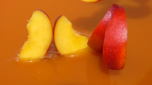 Кусочки персиков падают с брызгами в сок — стоковое видео