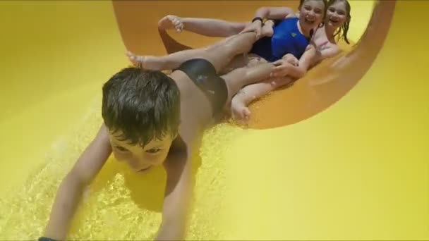 快乐的孩子们骑着马在一个水上公园里滑行着黄色的橙色滑梯 — 图库视频影像
