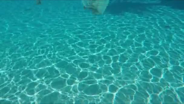 Pojken i simglasögon dyker i poolen och viftar med handen mot kameran. — Stockvideo