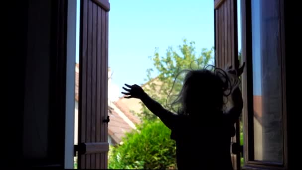 Silueta de una niña feliz saltando sobre la cama junto a la ventana abierta — Vídeo de stock