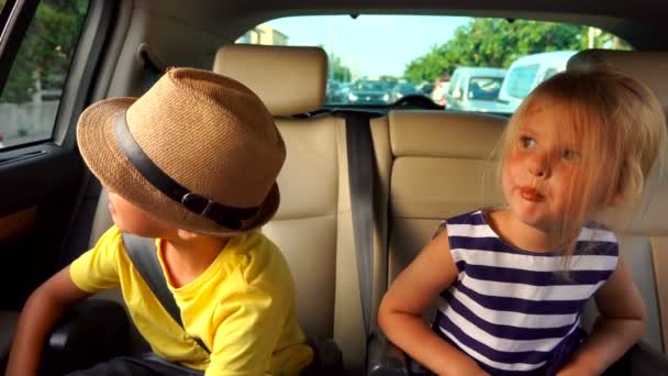 Kleine jongen en een meisje kijken door het raam in de auto op de achterbank — Stockvideo