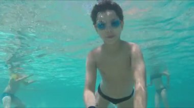 Yüzme gözlüklü siyah saçlı çocuk suyun altında dalıp yüzüyor. 