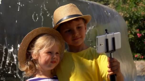 Malý chlapec a dívka dělají selfie na smartphone na pozadí fontány — Stock video