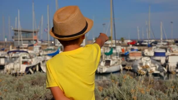 Liten pojke i hatt tittar på kajen i yacht hamnen — Stockvideo