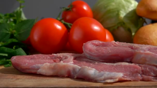 Filete de cerdo está cayendo en una tabla de madera en el fondo de verduras frescas — Vídeos de Stock