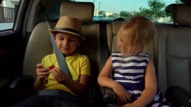 Küçük bir çocuk ve şapkalı sarışın bir kız arabanın arka koltuğunda oynuyorlar. 