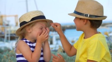 Küçük çocuk, sevimli bir kıza hasır şapka takması için yardım ediyor.