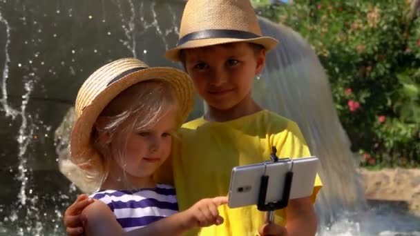 Little boy and girl in straw hats are making selfie on smartphone — Stock Video