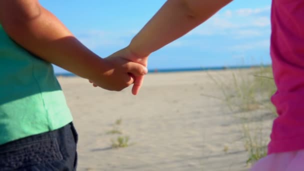 Крупный план мальчика и девочки в розовой юбке, держащихся за руки на пляже — стоковое видео
