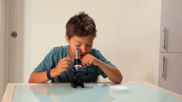 Curieux adolescent aux cheveux bruns regarde à travers un microscope — Video