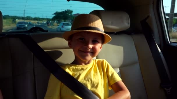 Little boy in hat is riding in the car at the backseat and smiling — Stock Video