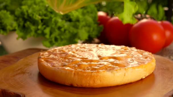 Свежий зеленый лист салата падает на булочку с гамбургером, смазанную горчицей — стоковое видео