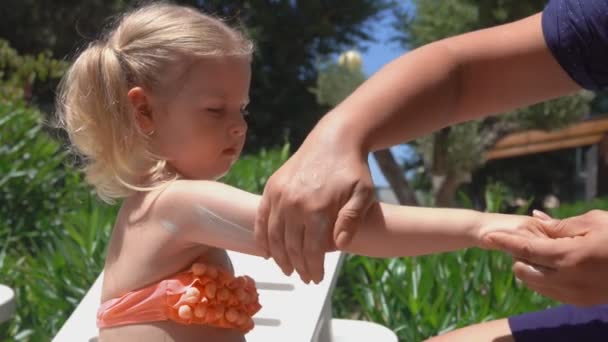 La mano spalma la crema protettiva solare sulla mano e sulle spalle della bambina — Video Stock