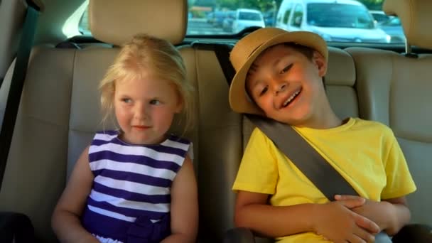 El niño y una niña están montando en el coche en el asiento trasero y sonriendo felizmente — Vídeos de Stock