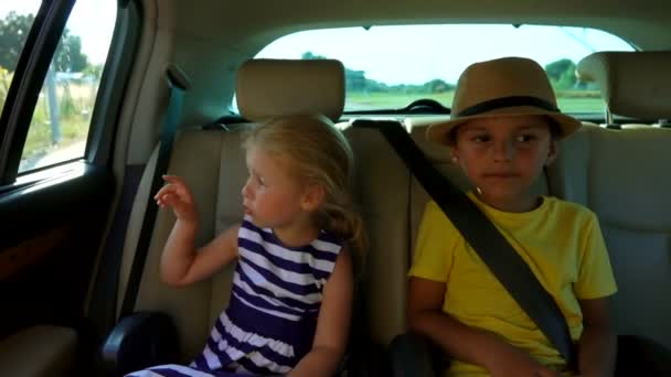 Niño y niña están montando en el asiento trasero y apuntando a la ventana del coche — Vídeos de Stock