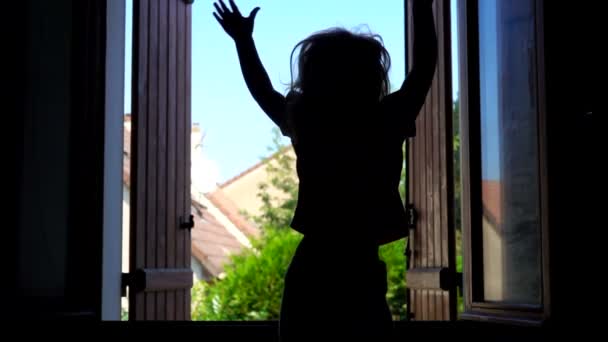 Silhuett av liten glad flicka viftar med händerna på bakgrunden av ett fönster — Stockvideo