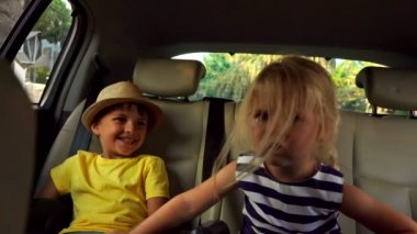 Küçük bir oğlan ve sarışın bir kız arabanın arka koltuğundalar.