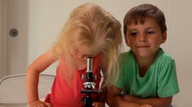 Oğlan kameraya bakarken tatlı bir kız mikroskoptan bakıyor.